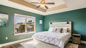 A bedroom with a bed, a ceiling fan, a window, and a nightstand. - Joy's Beach Retreat (Pensacola)