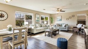 A spacious living room with a dining area, large windows, and a ceiling fan. - Joy's Beach Retreat (Pensacola)