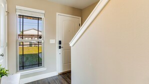 A hallway with a door, a window with a view of a house, and a plant. - Joy's Beach Retreat (Pensacola)