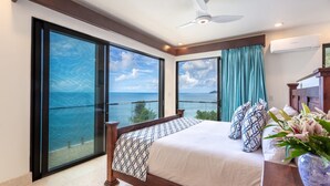 A bedroom with a large bed, a ceiling fan, and a view of the sea.