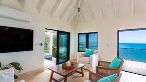 A spacious living area with a large flat-screen TV, comfortable seating, and a view of the ocean.