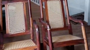 Two wooden chairs with woven seats and backs, positioned in a room with a white wall and a radiator in the background. - Wenmel Home (San Andrés)