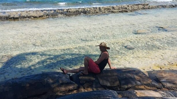 A person sitting on a rock by a clear beach with a view of the ocean. - Wenmel Home (San Andrés)