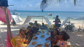 A group of people dining at a beachside table with a view of the ocean and boats in the background. - Wenmel Home (San Andrés)