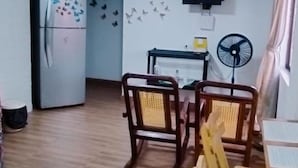 A compact kitchen with a refrigerator, wooden chairs, a dining table, and a wall-mounted fan. - Wenmel Home (San Andrés)