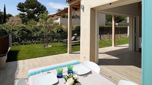 An outdoor patio with a table set for four, surrounded by a garden and a building with a tiled roof. - Bungalow with terrace close to the Gigaro beach (LA CROIX VALMER)