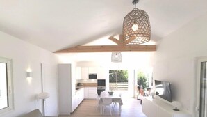 A modern living room with a sofa, a dining area with chairs, a kitchen with white cabinets, and a TV on a white cabinet. - Bungalow with terrace close to the Gigaro beach (LA CROIX VALMER)