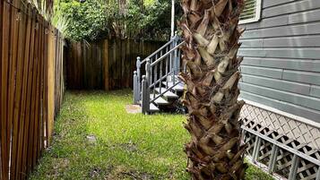 A backyard with a staircase leading to a porch, a palm tree, and a wooden fence.