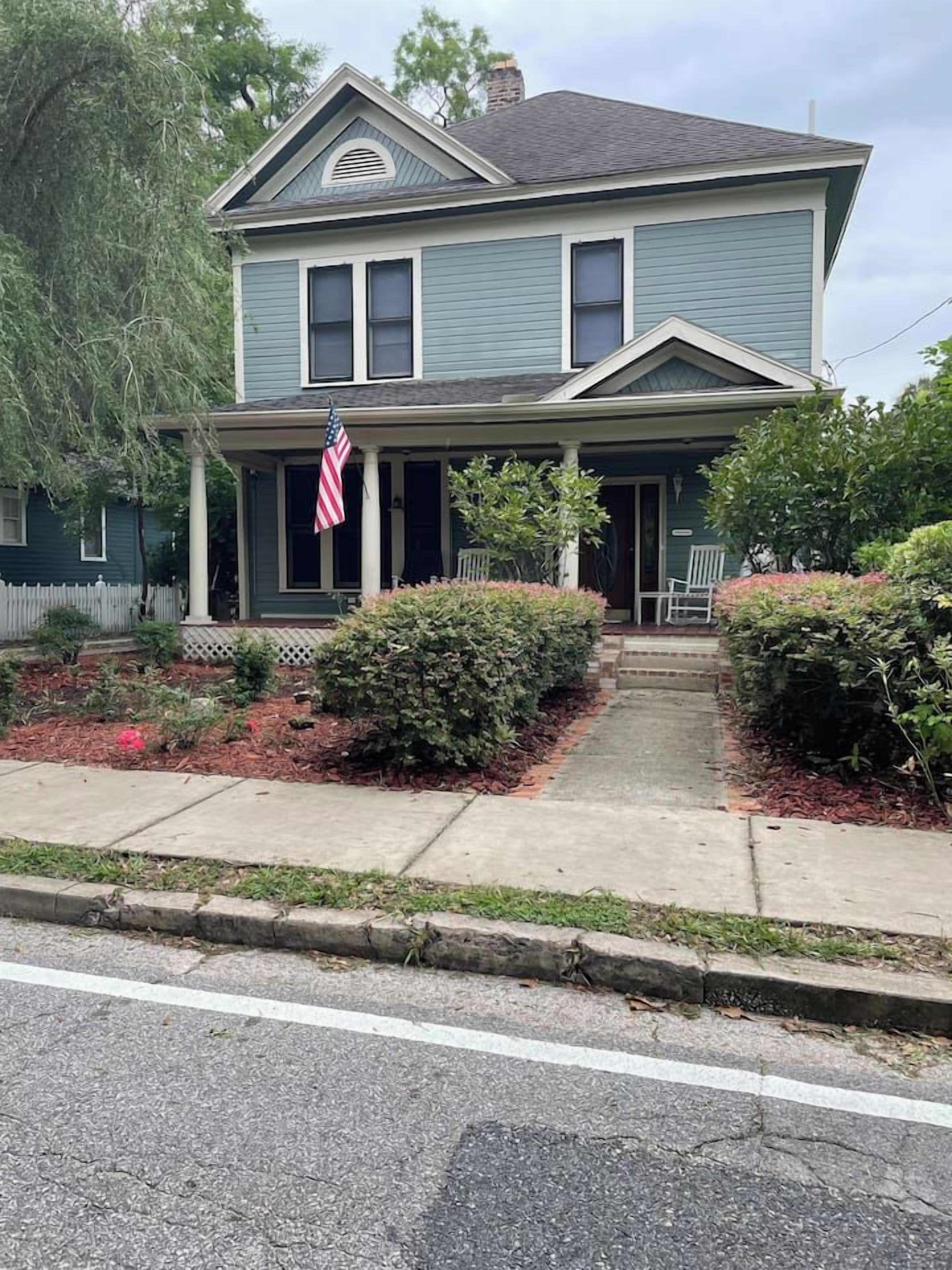 A two-story house with a porch, a flag, and a front yard.