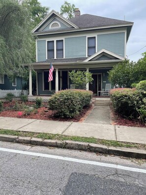 A two-story house with a porch, a flag, and a front yard.