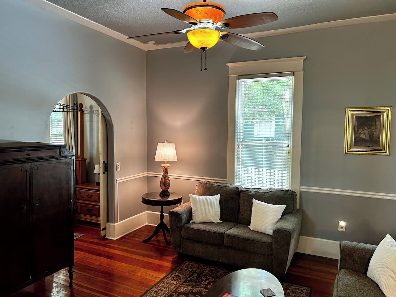 A living room with a ceiling fan, a sofa with cushions, a lamp, and a window with blinds.