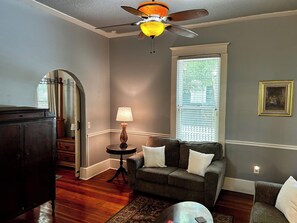 A living room with a ceiling fan, a sofa with cushions, a lamp, and a window with blinds.
