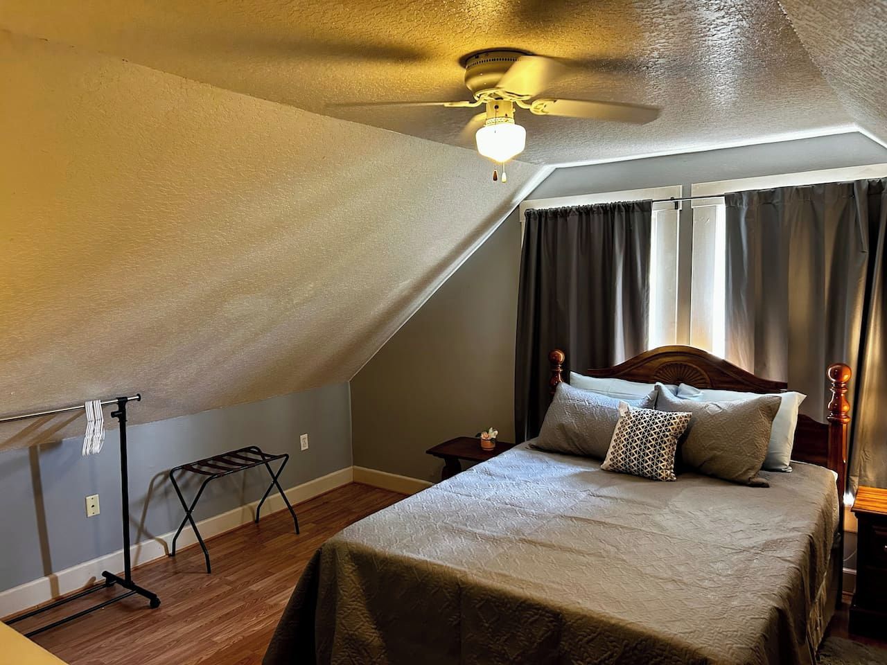 A bedroom with a sloped ceiling, a bed with multiple pillows, a nightstand, a small table, and a ceiling fan.
