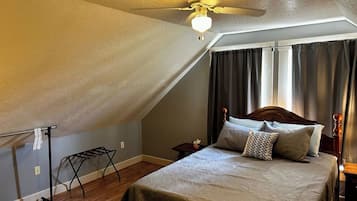 A bedroom with a sloped ceiling, a bed with multiple pillows, a nightstand, a small table, and a ceiling fan.