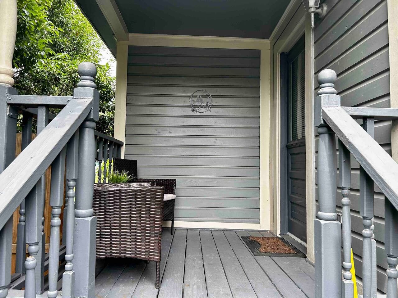 A wooden deck with a wicker bench and a small table, a gray door, and a mailbox.