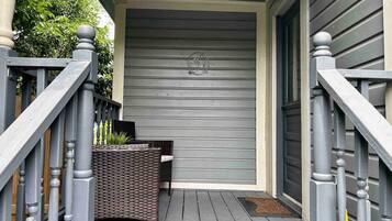 A wooden deck with a wicker bench and a small table, a gray door, and a mailbox.