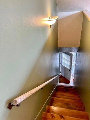 A wooden staircase with a handrail, a light fixture on the wall, and a door at the top.