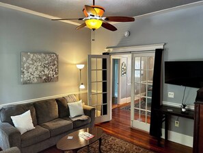 Un salon comprenant un canapé, une table basse, un ventilateur de plafond, des œuvres d’art et un téléviseur.