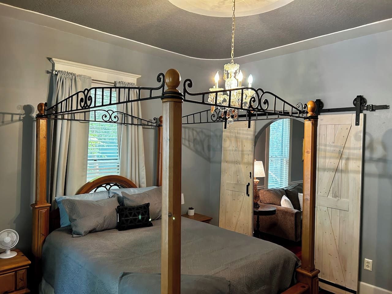 Un lit à baldaquin surmonté d’un lustre, une armoire en bois et une petite table avec une lampe.