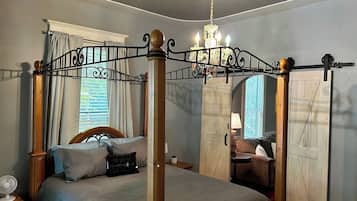 Een hemelbed met een kroonluchter, een houten garderobe en een klein tafeltje met een lamp.