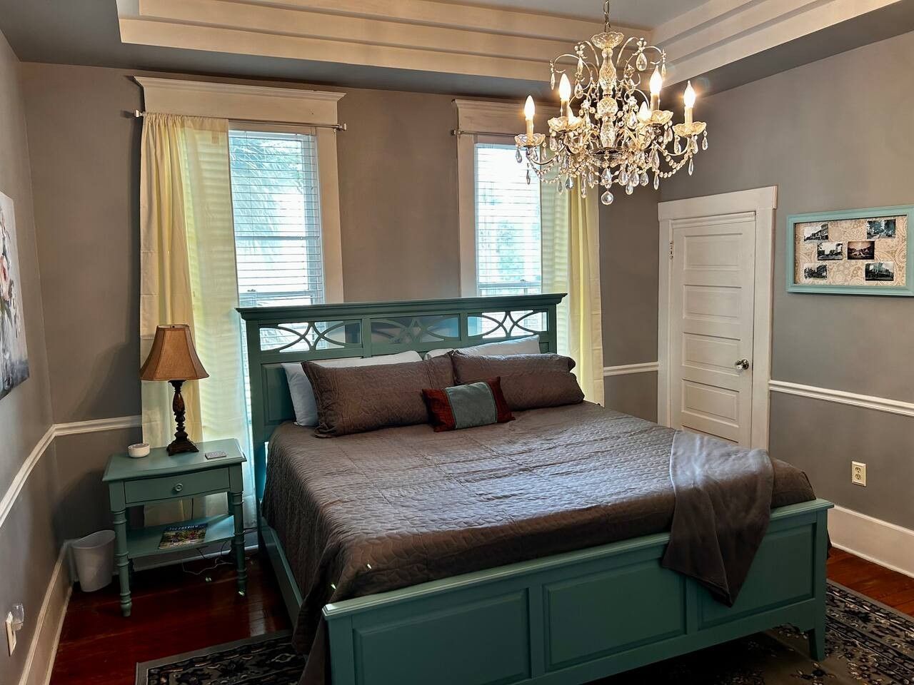A bedroom with a bed, a nightstand, a lamp, a chandelier, and a door.