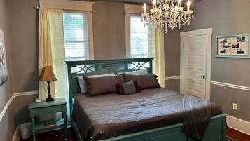 A bedroom with a bed, a nightstand, a lamp, a chandelier, and a door.