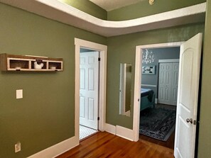 A hallway with a wooden floor, a white door, and a small shelf with decorative items.