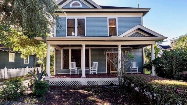 A two-story house with a porch, a picket fence, and a well-maintained garden.