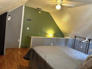 Une chambre à coucher avec un lit, un ventilateur de plafond, un luminaire et un mur vert.
