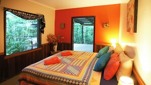 A bedroom with a large bed, colorful pillows, a nightstand with a lamp, and a window with a view of greenery. - Tropical Bliss BNB (Utchee Creek)