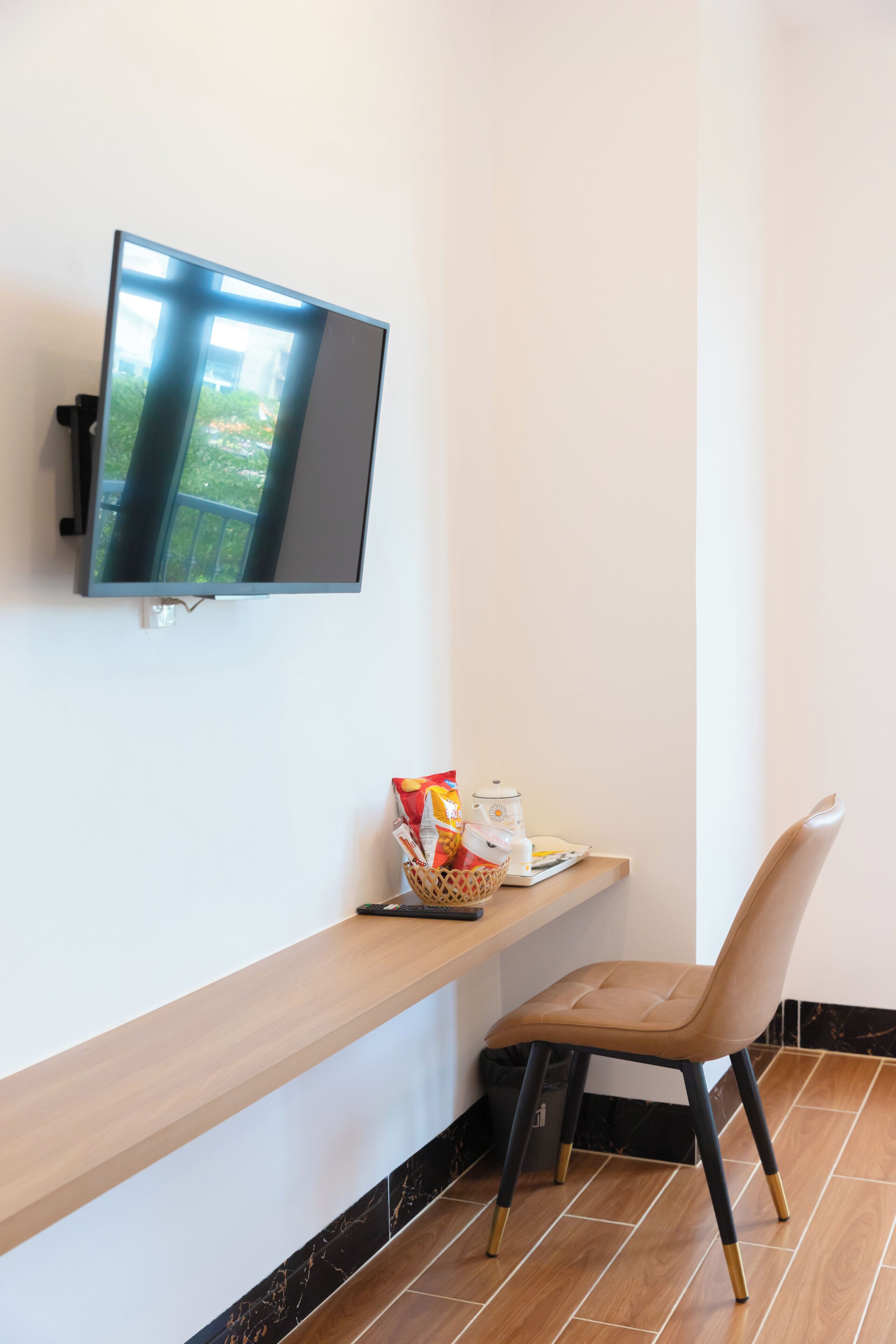 A modern room with a flat-screen TV mounted on the wall, a wooden shelf with snacks, and a chair.