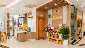A hotel reception area with a wooden reception desk, a sunburst decoration, and a sign that reads "Sunrise Hotel." - SUNRISE Hotel Bac Lieu (Bac Lieu)