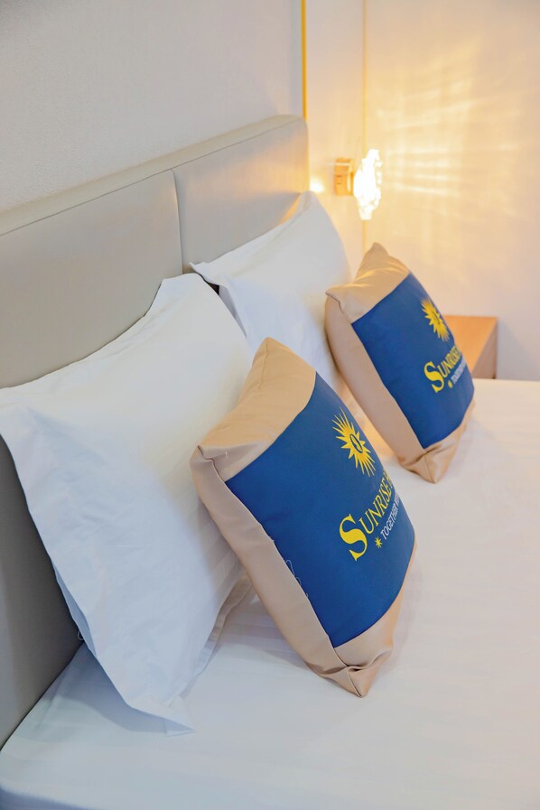A bed with two pillows, one white and one with a blue and beige design featuring a sun and text.