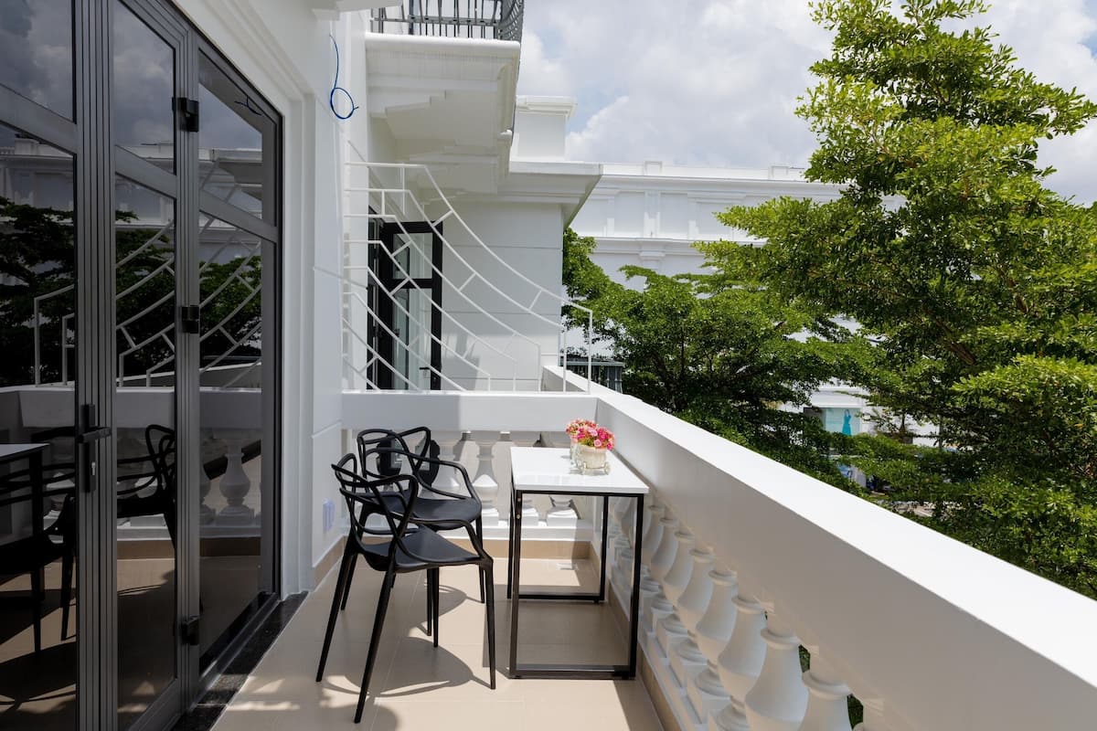Uma varanda com mesa e cadeiras, grade branca e vista para árvores e edifícios.