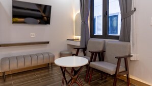 A modern living room with a sofa, two chairs, a small table, a TV mounted on the wall, and a window with curtains. - SUNRISE Hotel Bac Lieu (Bac Lieu)