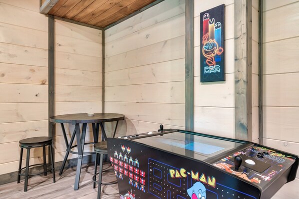 Une table de billard avec un néon, deux tabourets et une table avec un plateau en verre, le tout dans une pièce aux murs en bois.