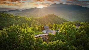 Un chalet de montagne entouré d’une forêt dense, offrant une vue dégagée sur les collines environnantes et un coucher de soleil en toile de fond.