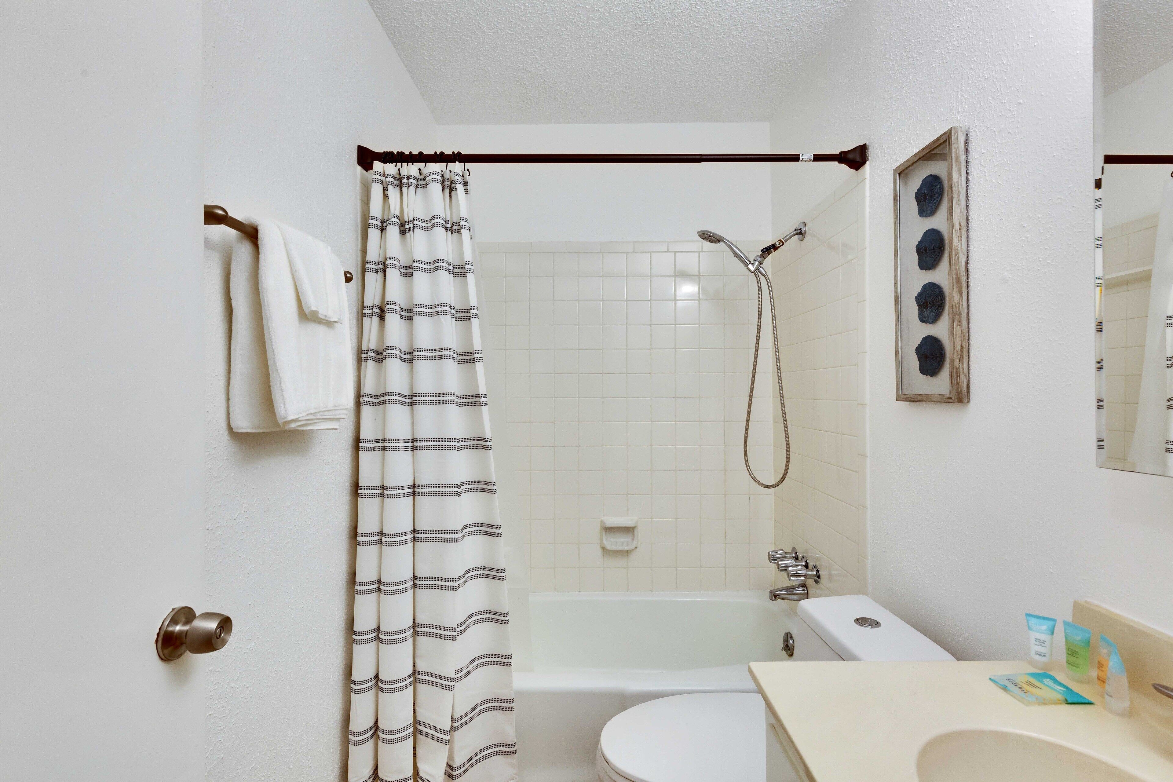 A bathroom with a shower, toilet, sink, and a towel rack.