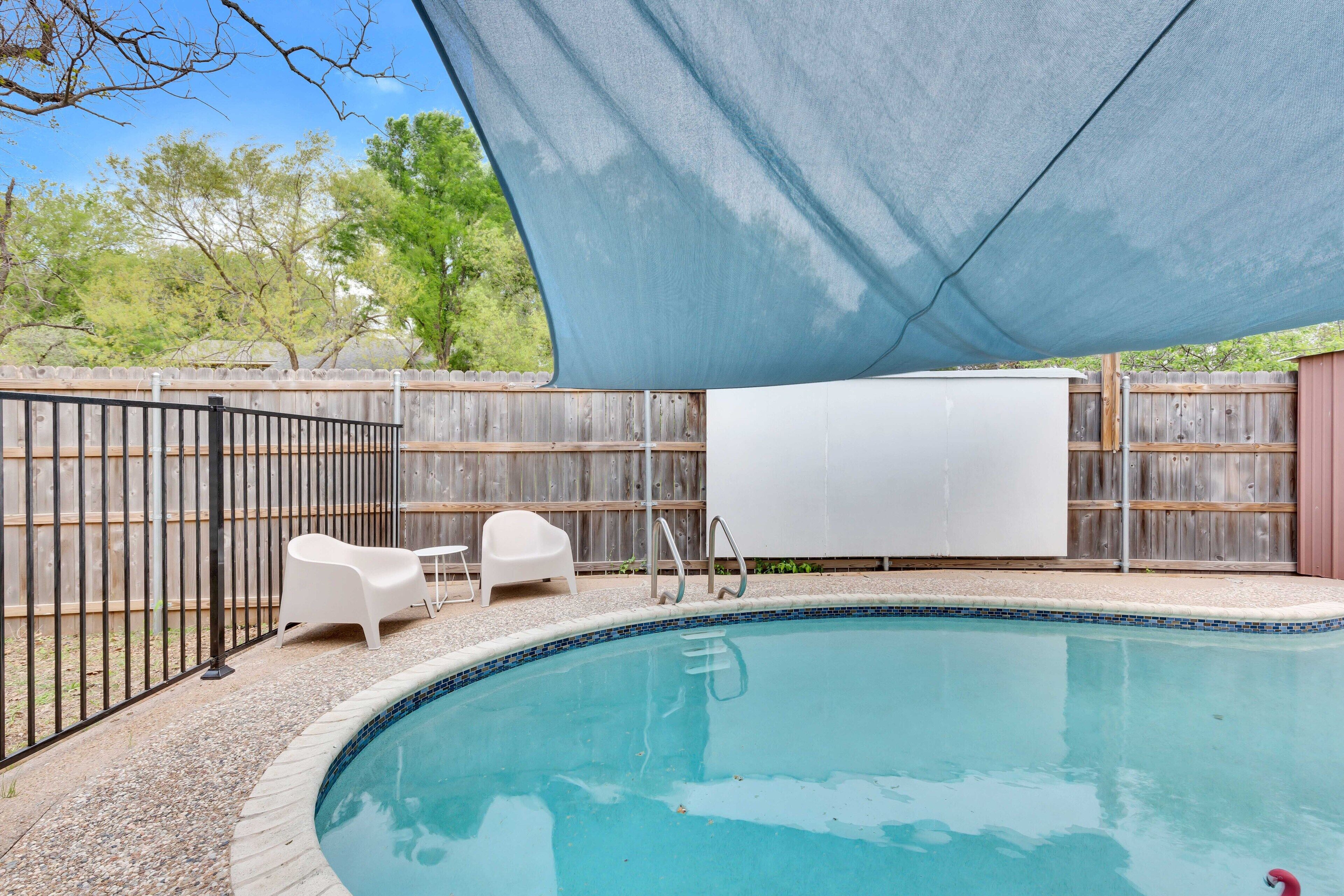 A backyard with a swimming pool, a shaded area, and a wooden fence.