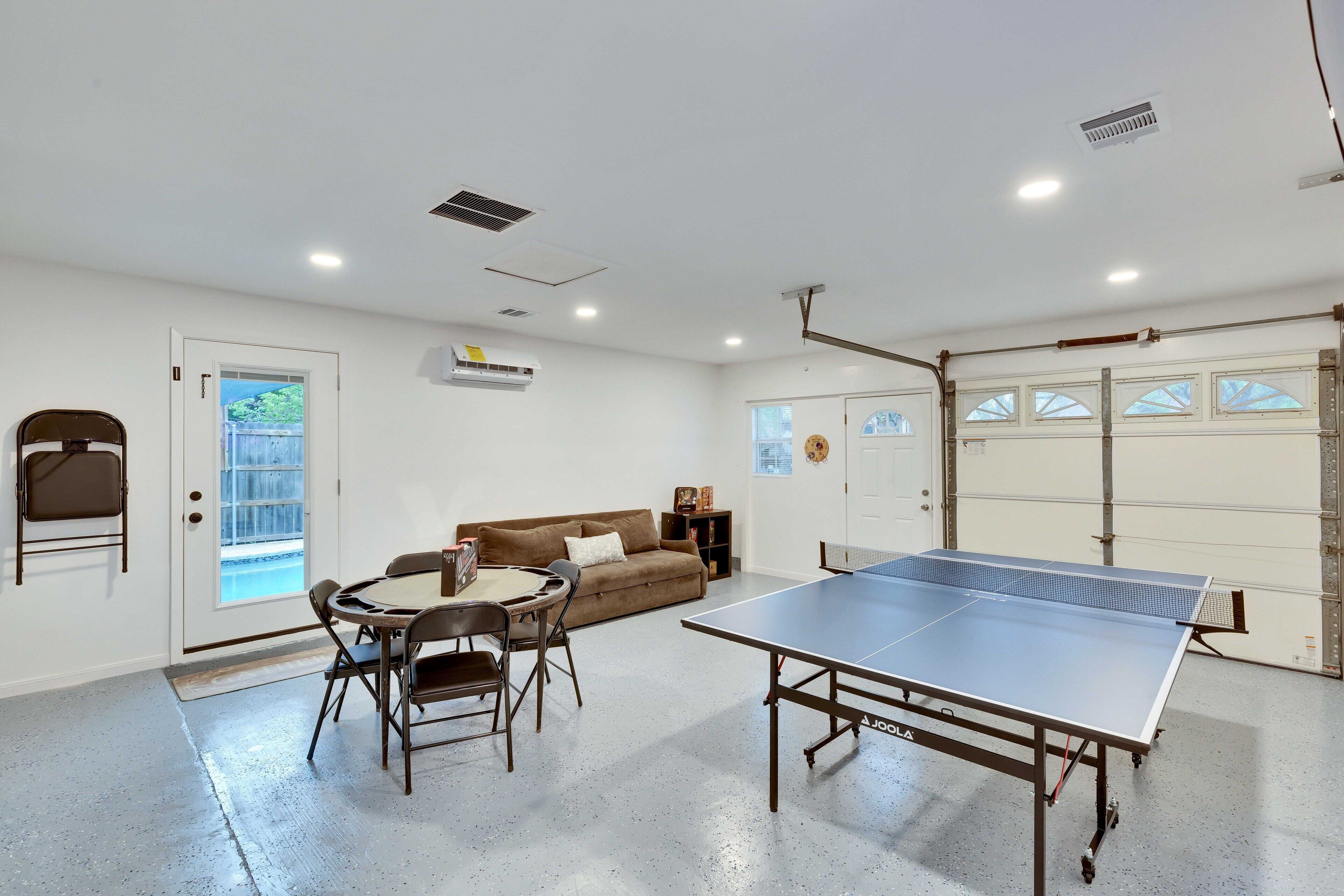 A room with a ping pong table, a sofa, a dining table with chairs, and a door leading outside.