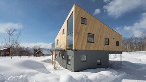 A modern house with a wooden exterior and large windows, surrounded by snow. - Niseko Village ski Chalet 4BDR Car Delica Included (niseko)