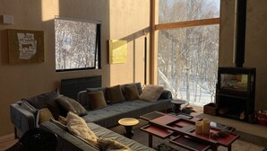 A cozy living room with a large window, a fireplace, and a sofa with cushions. - Niseko Village ski Chalet 4BDR Car Delica Included (niseko)
