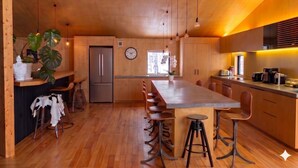 A modern kitchen with wooden cabinets, a central island with stools, a refrigerator, and a clock on the wall. - Niseko Village ski Chalet 4BDR Car Delica Included (niseko)