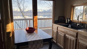A kitchen with a wooden table, a red bowl, and a view of mountains through large windows. - Located close to Tanalian River, amazing views and cozy setting. (Port Alsworth)