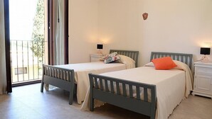 Ein Schlafzimmer mit zwei Einzelbetten, einem Nachttisch mit Lampe und einer Glastür zum Balkon.