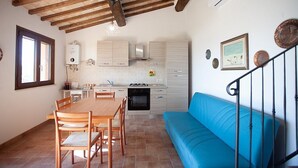 A kitchen with wooden beams, a dining table with chairs, a blue sofa, and a staircase.