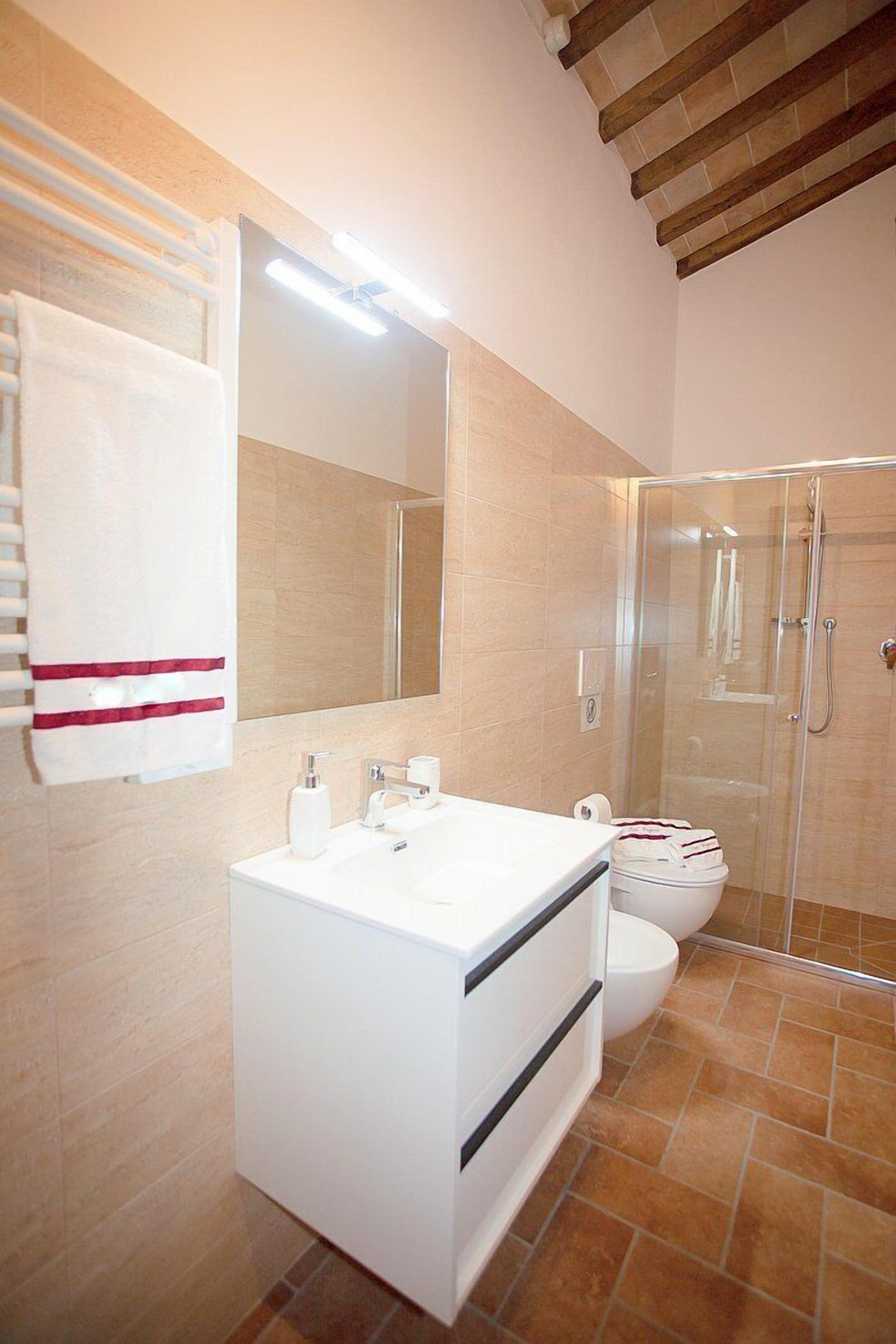 A modern bathroom with a white vanity, a large mirror, a glass shower enclosure, and a toilet.