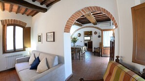 A living room with a sofa, a dining table, and a kitchen area visible through an archway. - Casa Fattorina F: A characteristic and welcoming two-story independent house surrounded by the greenery, with Free WI-FI. (Chiusi)