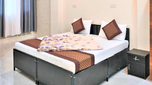 A bedroom with a bed, a nightstand, a ceiling fan, and a window with curtains. - Comfort Inn Hotel.Near MayurVihar Metro1 (New Delhi)