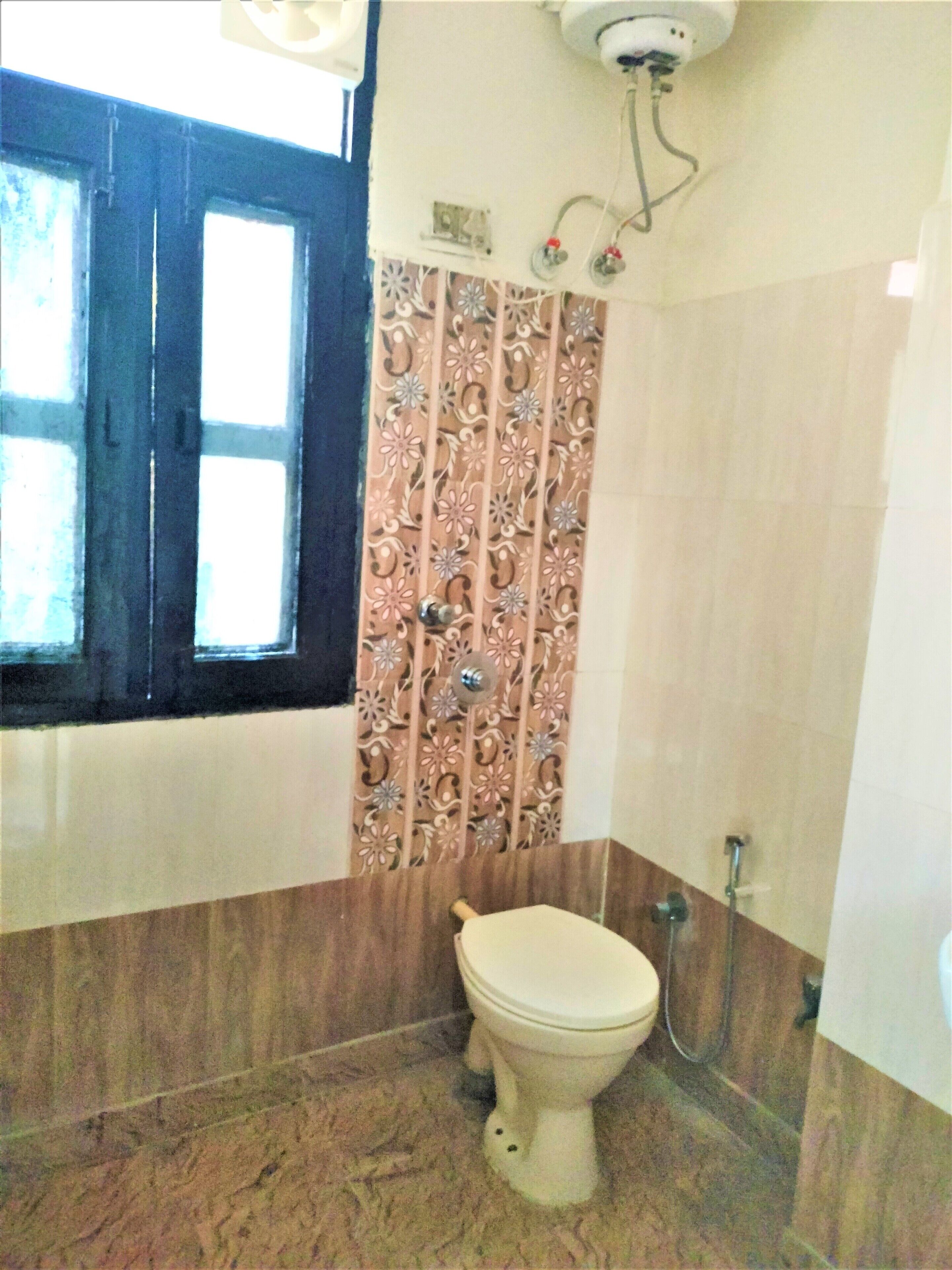 Un baño con inodoro, ducha y ventana con marcos de madera oscura.